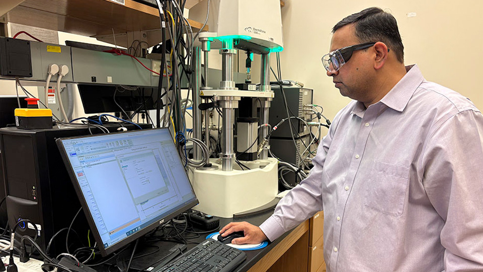 A researcher using a computer workstation to operate a mechanical testing instrument in a lab.